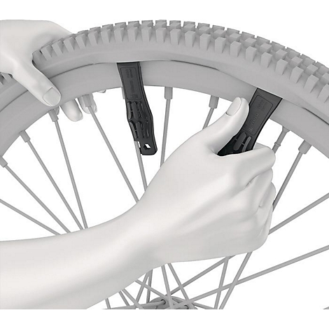 Hände montieren einen Reifen auf einer Fahrradfelge mit Reifenhebern. Das Bild zeigt das Detail der Arbeit.