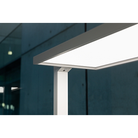 Close-up van een moderne, helder verlichte bureaulamp. De lichtbak is rechthoekig en wit, het frame is wit en hoekig.