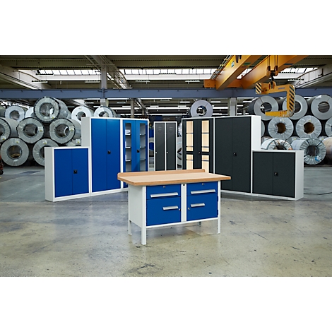 Eine Werkbank und verschiedene Metallschränke in blau und anthrazit stehen in einer Fabrikhalle.