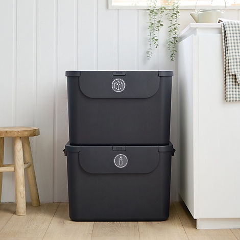 Person wirft Flasche in schwarzen Müllbehälter. Der Behälter steht auf einem weissen Mülleimer in einer Küche.