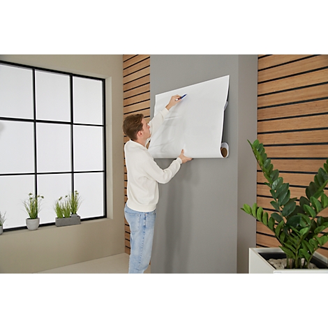 A man attaches a roll of paper to the wall, describing it with a blue pen.