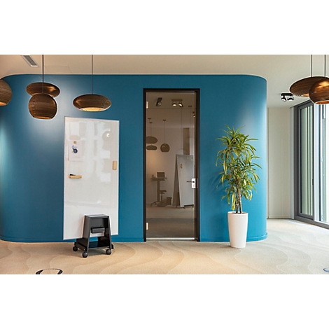 Un espace de bureau avec un mur turquoise, une paroi vitrée, des plantes et des lampes. Un tableau blanc est posé sur un tabouret roulant.