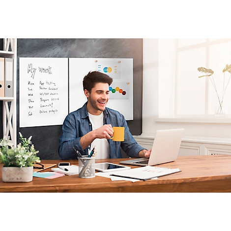 Een lachende man zit aan een bureau te werken op een laptop. Hij houdt een gele mok vast.