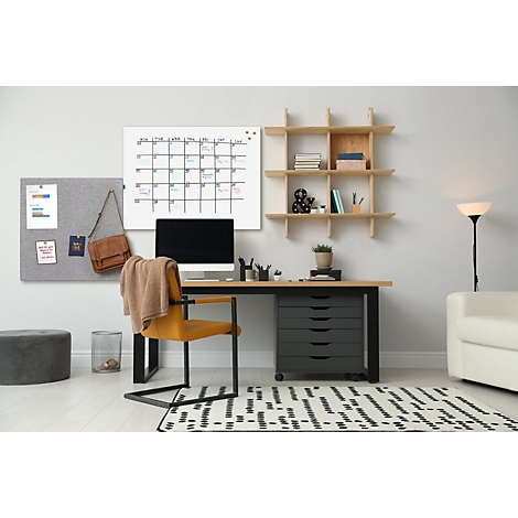 Ein gemütlicher Arbeitsplatz mit Schreibtisch, Kalender, Pinnwand und Stuhl. Auf dem Schreibtisch steht ein Computer und eine Pflanze.