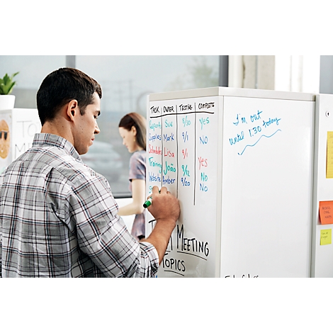 Een man schrijft met een groene stift op een whiteboard muur, terwijl een vrouw op de achtergrond staat. Op het bord staan lijsten en notities.