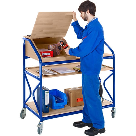 A man in blue overalls opens a serving cart. There are tools and accessories on the cart.