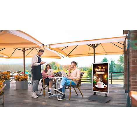 Een ober neemt de bestelling op. Twee mensen zitten aan een tafel, een van hen met een laptop. Op de voorgrond een reclamebord met een koffiemotief.