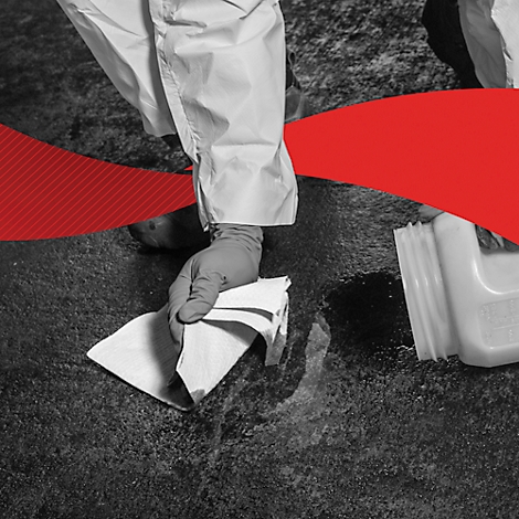 Person in protective clothing wiping up liquid with a cloth. Next to it a container.