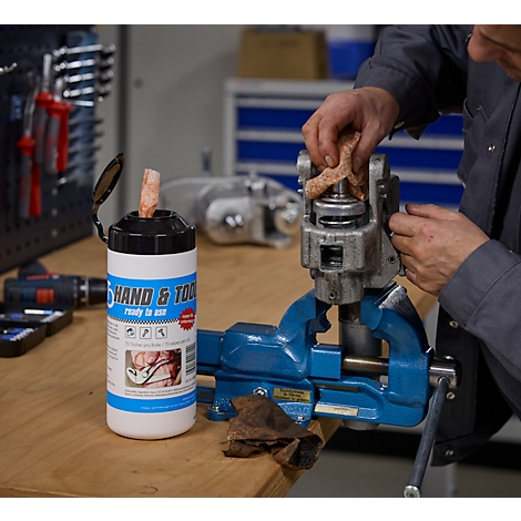 Een man maakt een metalen mechanisme schoon op een bankschroef. Daarnaast staat een flesje schoonmaakdoekjes.