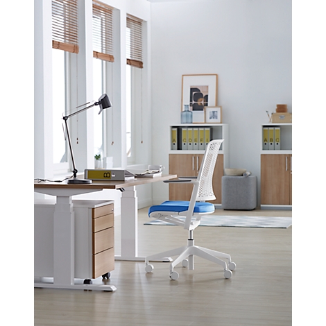 Bright office room with desk and white chair. Windows with blinds and light wooden floor. There is a lamp on the table.