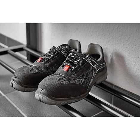 Black work shoes with laces, resting on a metal shoe rack, leaning against a wall.