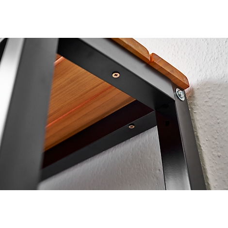Close-up of a black metal structure with brown wooden panels, screws and a light wall.