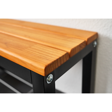 Close-up of a wooden bench with black metal legs. The seat consists of light brown wooden boards. A silver screw is located at the corner.