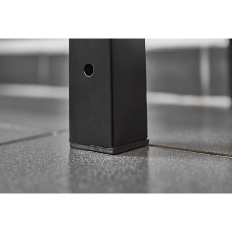 Close-up of a black metal leg with a hole, standing on gray tiled flooring.