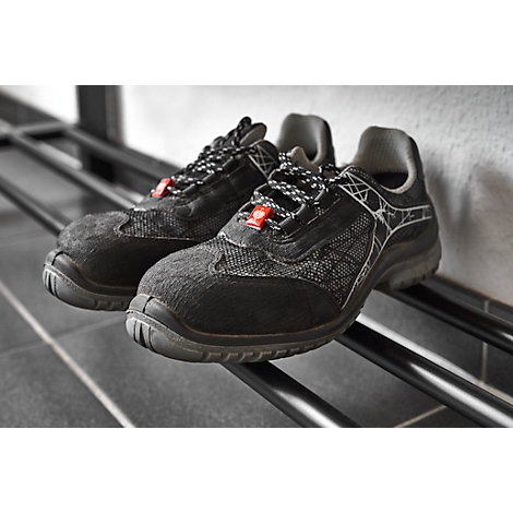 Black safety shoes with red details are on a black shelf.