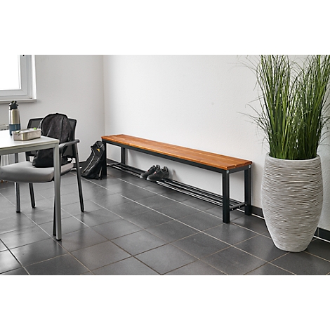 Wooden bench with black frame and shelf. Next to it, a large plant in a decorative pot.