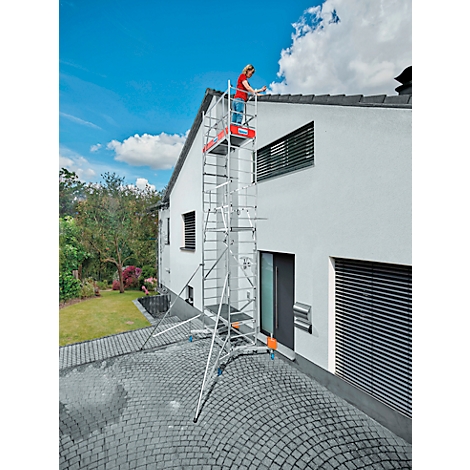 A person stands on scaffolding working on a house roof. Blue sky with clouds in the background.