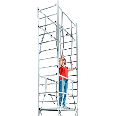 A woman in a red top stands on scaffolding, holding on. She's looking up.