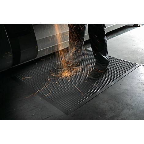 Man stands on a black, studded mat. Sparks are flying during the work.