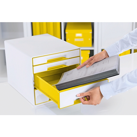 Hands placing files in a yellow drawer of a white cabinet. More yellow boxes in the background.