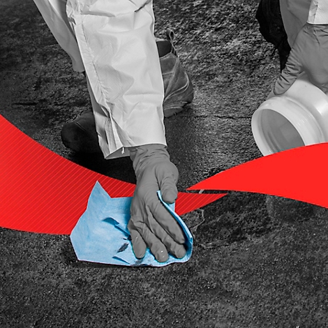 Personne en combinaison de protection essuie avec un chiffon bleu sur un sol gris. Bande rouge encadrant l'image.