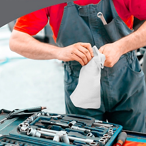 Ein Mechaniker hält einen weißen Stoffhandschuh. Werkzeugkasten und eine Schraubenschlüssel sind im Hintergrund zu sehen.