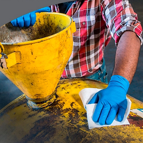 Ein Mann in rot-kariertem Hemd reinigt mit einem blauen Handschuh und einem Tuch ein gelbes Gerät.
