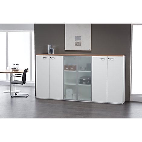 White cabinet with glass and wood doors. A table with chairs in the background. A picture hangs on the wall.