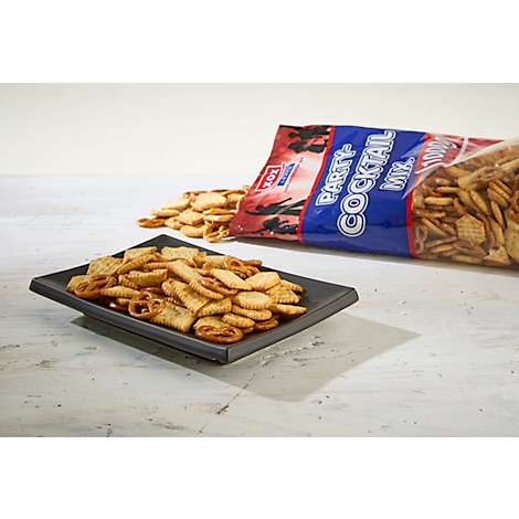 Ein Teller Party-Cocktail-Mix mit einer Tüte im Hintergrund. Einige Snacks liegen verstreut.