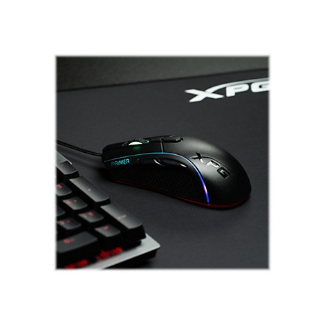 Schwarze Gaming-Maus mit LED-Beleuchtung liegt auf schwarzer Unterlage neben Tastatur. Auf der Maus steht "PRIMER" und "XPG".