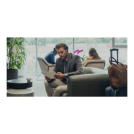 Ein Mann im Anzug sitzt und schaut auf ein Tablet. Im Hintergrund sitzen weitere Personen.