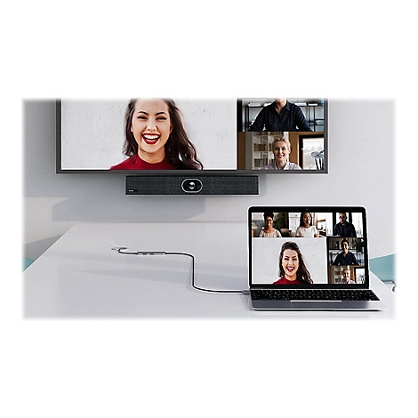 Frau in Videokonferenz, Blick auf einen Bildschirm. TV mit Lautsprecherleiste, Laptop mit Teilnehmern. Auf Tisch liegendes Kabel.