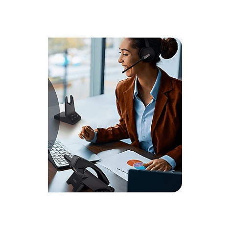 Eine Frau mit Headset arbeitet am Schreibtisch. Sie betrachtet Diagramme und einen Laptop.