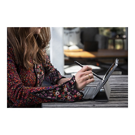 Une femme travaillant sur une tablette avec un stylet, portant un manteau fleuri et une bague en or.