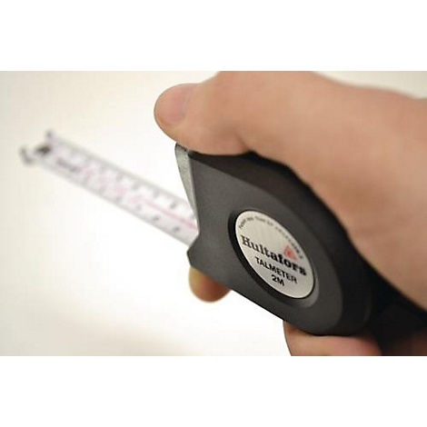 Een hand houdt een zwarte rolmaat vast. Op de rolmaat staat "Hultafors TALMETER 2M".