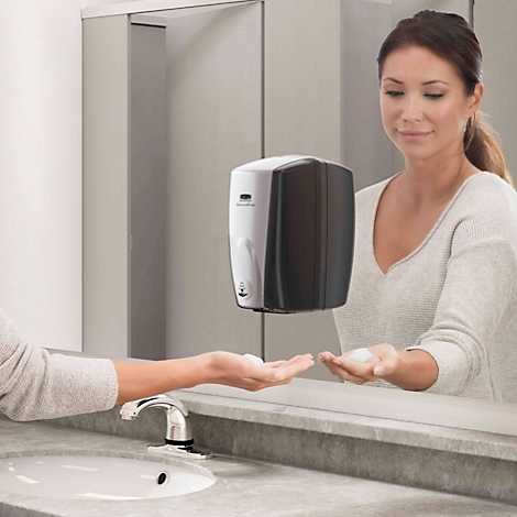 Een vrouw wast haar handen met zeep uit een contactloze zeepdispenser. Ze glimlacht terwijl het schuim in haar handpalm valt.