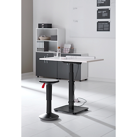 Een in hoogte verstelbaar bureau met een kruk in een kantoor. Er liggen documenten en een waterfles op de tafel.