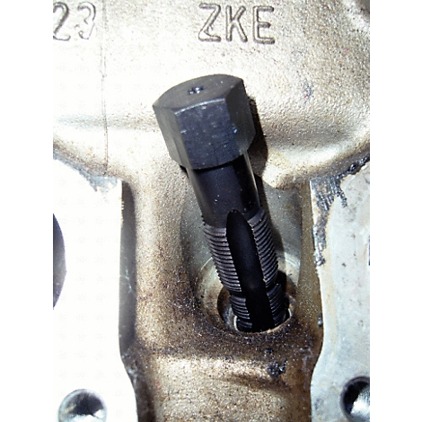 Nahaufnahme eines schwarzen Werkzeugs, das in eine Bohrung eingesetzt ist. Im Hintergrund ist ein metallischer Untergrund mit der Aufschrift "ZKE" zu sehen.