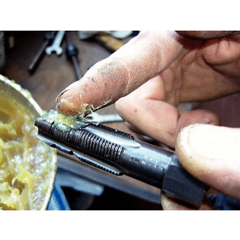 Hand schmiert Metallwerkzeug mit gelbem Fett. Werkzeug ist in Nahaufnahme, daneben Schmierfett.