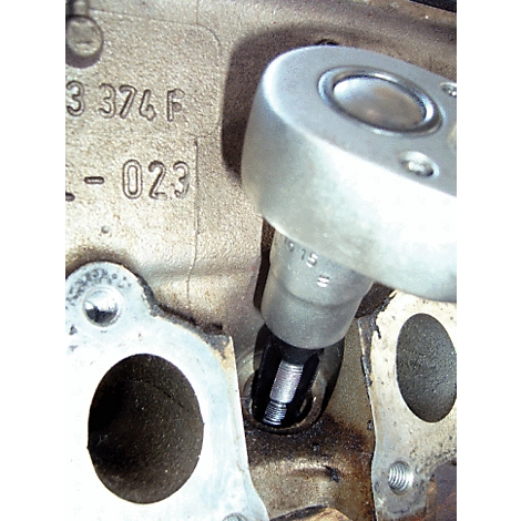 Eine Nahaufnahme zeigt eine Ratsche, die einen Bolzen in ein Motorteil schraubt. Auf dem Motorteil sind Zahlen eingraviert.