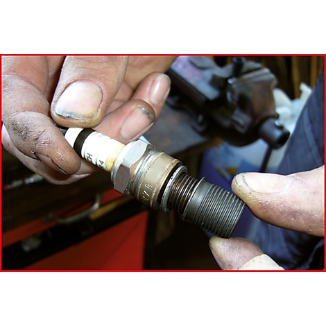 Nahaufnahme einer Person, die eine Zündkerze in den Händen hält. Der Fokus liegt auf der Zündkerze und den Fingern.