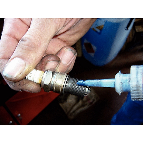 Nahaufnahme einer Hand, die eine Zündkerze hält und blaues Schmiermittel aufträgt.