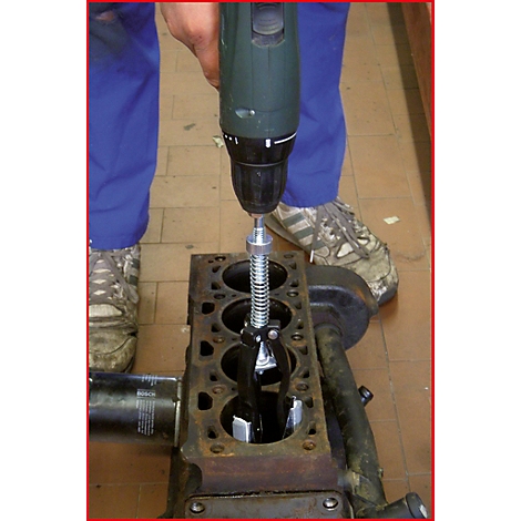 Ein Mechaniker benutzt einen Akkuschrauber, um einen Motorblock zu reparieren. Nahaufnahme des Werkzeugs und des Motorblocks.