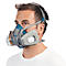 Homme portant un masque respiratoire. Masque gris et bleu avec filtres et sangles. Vue de face, fond blanc.