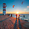 Lighthouse with red and white stripes, pier and kitesurfers at sunset.