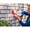 A woman is mounting something on a brick wall with red pliers.