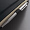 Gros plan d'un cahier avec une couverture noire et un stylo argenté. Le stylo est inséré dans la couverture.