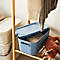 Blue storage box with lid, filled with knitwear, stands on a wooden rack. Clothing hangs above.