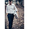 A man with a suitcase walks a path, serious look. He wears a shirt and pants.