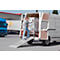 A woman is loading a white van with a metal cage. A loading ramp is unfolded.